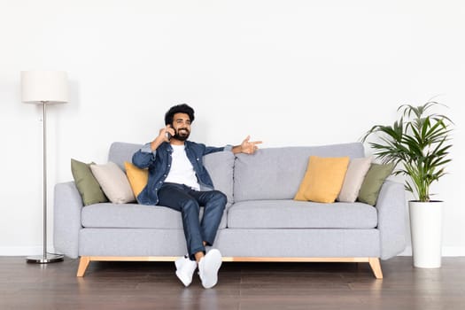 Positive young indian guy chilling on couch, have phone call