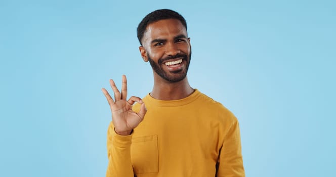 Happy, face and man with perfect hands in studio for support, review or success, vote or agree on blue background. Smile, portrait and male model show ok, emoji or yes, thank you or feedback results