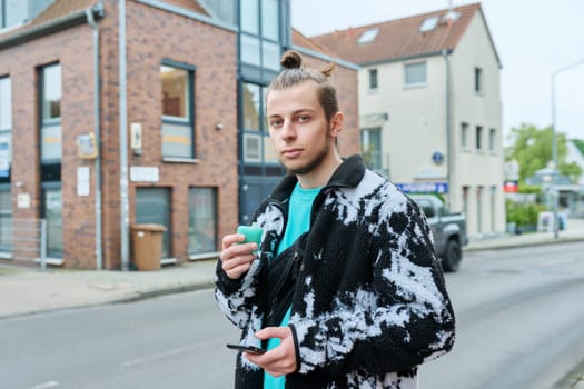 Young hipster male using smartphone, smoking disposable electronic cigarette