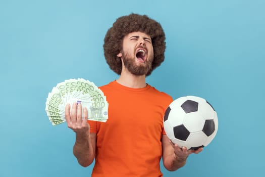 Man holding soccer ball and hundred euro bills, screaming with happiness, betting and winning.