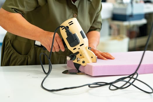 Hands of a furniture master cut a piece of foam with foam cutting machine