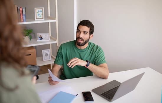 Calm millennial muslim man ceo with laptop talking to manager with documents