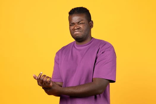 Black man suffering from wrist pain on yellow background
