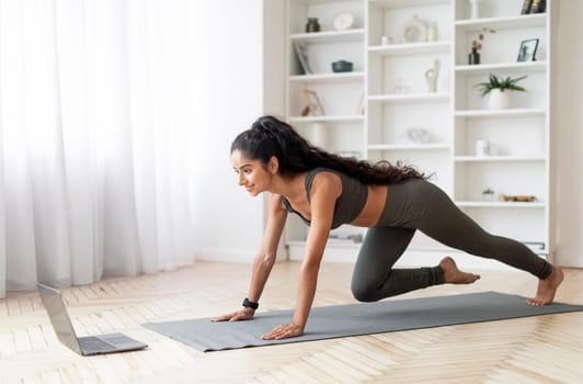 Happy Young Indian Fitness Lady Near Laptop Computer Standing In Plank Exercising In Living Room At Home. Domestic Online Training Concept. Sport And Technology, Copy Space