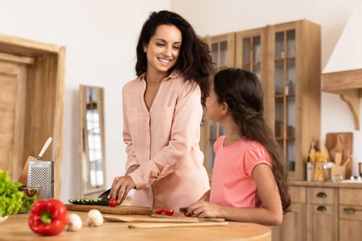 Mommy and little daughter engaging in cooking vegetable salad together at home kitchen, both displaying cheerful interactions, promoting healthy eating habits and nutritious home cooked meals