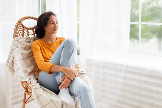 Arab woman in casual sits in comfortable wicker armchair indoors