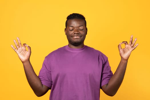 Calm african guy doing meditation with om gesture, yellow background