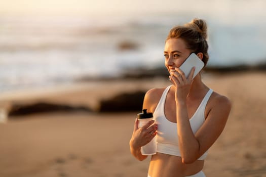 Young woman chatting on phone, post-yoga, beach sunset