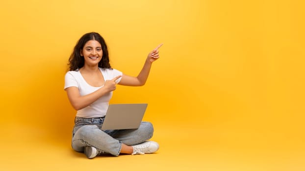 Happy young indian woman with laptop pointing at copy space