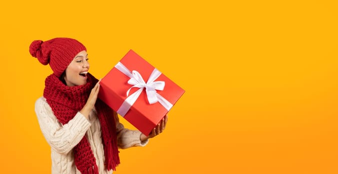 Cheerful woman posing with Xmas present box on yellow backdrop