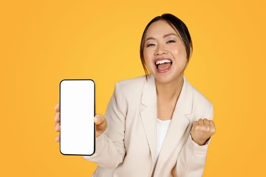 Satisfied chinese millennial lady in suit, show smartphone with empty screen, enjoy win