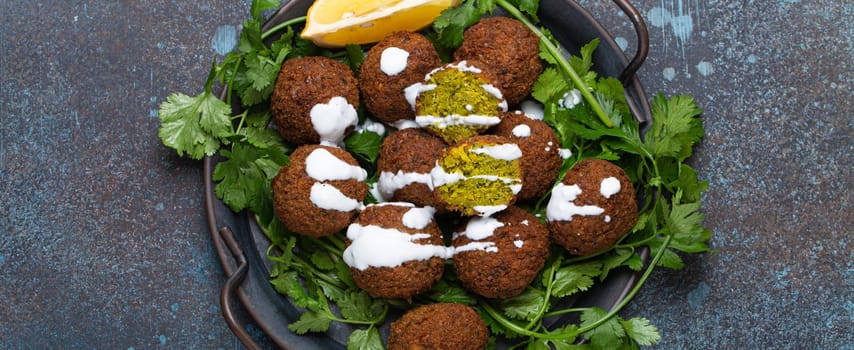 Plate of fried falafel balls served with fresh green cilantro and lemon, top view on rustic concrete background. Traditional vegan dish of Middle Eastern cuisine