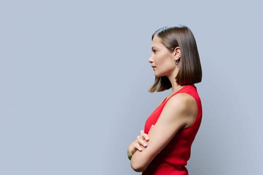 Profile view of young fashionable woman in red on gray background