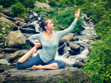 Sorty fit woman doing yoga asana outdoors at tropical waterfall