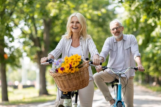 Happy cheerful mature couple enjoying bike ride in summer park