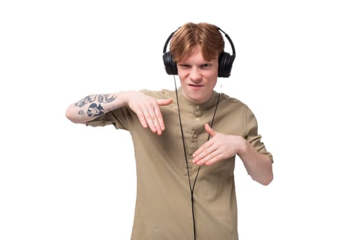 young red-haired man with glasses dressed in a brown shirt grimaces and listens to music on headphones