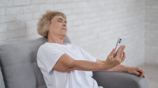 An elderly Caucasian woman suffers from farsightedness and tries to read a smartphone with her arm outstretched.