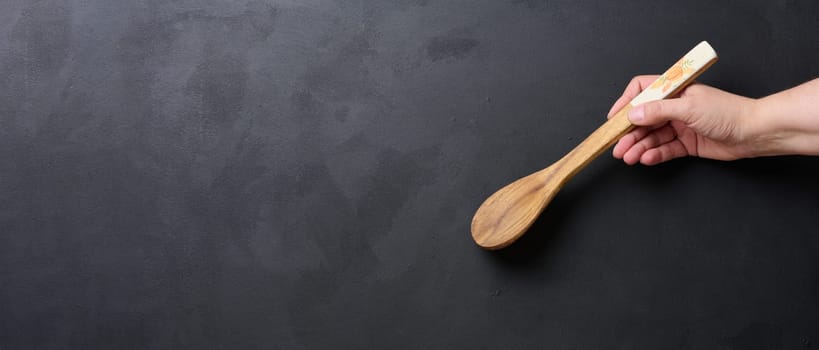 A woman's hand holds a wooden spoon on a black background, space for an inscription