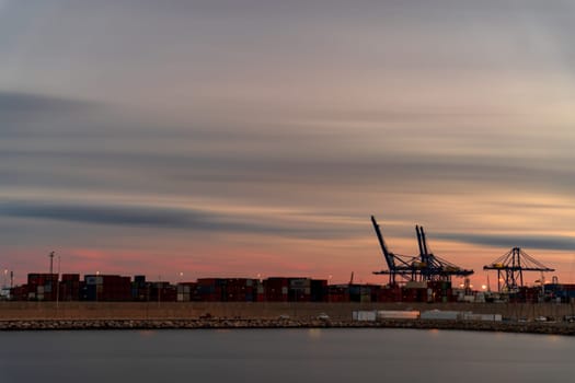 Bustling Commercial Dock at Dusk with Containers and Cranes