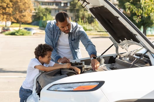 Black father and preteen son checking car engine outdoors
