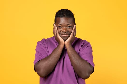 Contented Smiling Black Man Cupping Face In Hands, Yellow Background