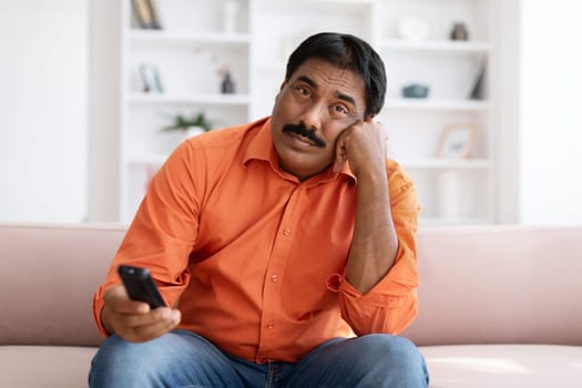 Bored Indian Man Watching TV Switching Channels With Remote Control