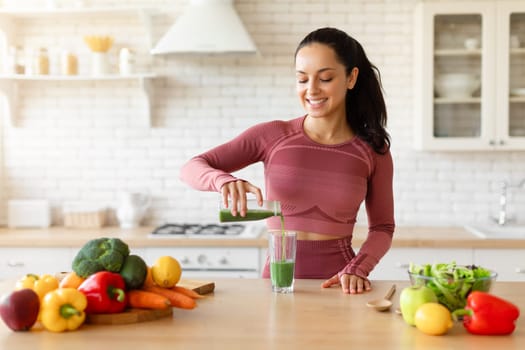 Happy Young Woman Pouring Green Smoothie In Glass At Home