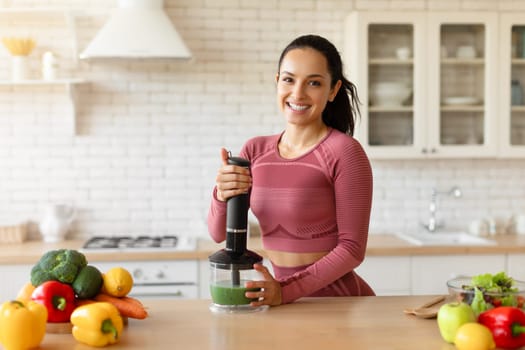Young woman preparing detox smoothie in blender on white kitchen
