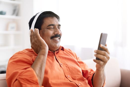 Positive mature indian man using phone and headphones