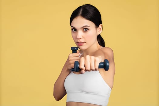 Determined woman in sportswear lifting dumbbells on yellow background