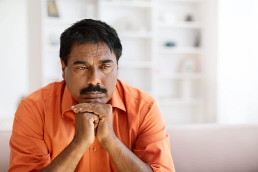 Closeup of depressed indian middle aged man sitting on couch