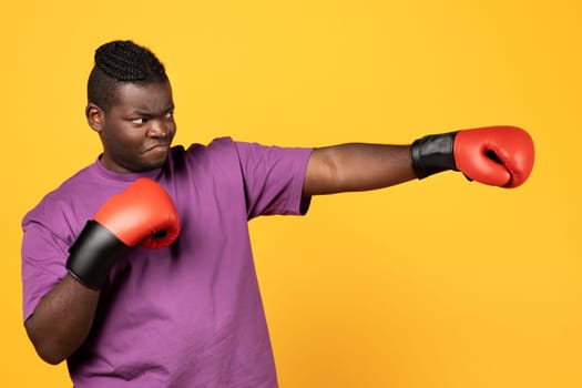 Black boxer guy throwing punch wearing boxing gloves, yellow background