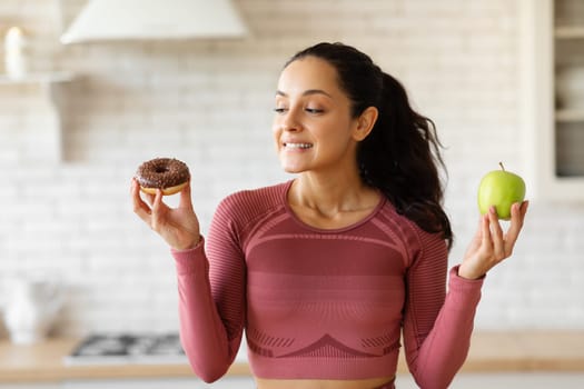 Athletic woman in activewear choosing apple fruit or donut indoor