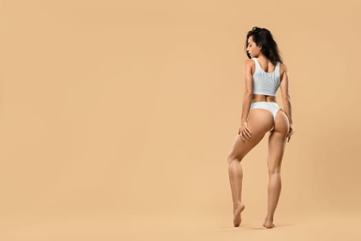 Perfect body shape. Woman posing in white underwear over beige studio background