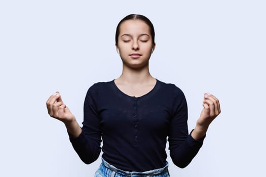 Teenage relaxed girl in headphones making meditation gesture with fingers