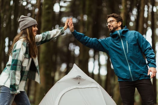 Positive young caucasian couple in jackets, enjoy travel vacation, make tent, give high five