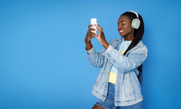 Stylish young african american lady 20s using phone and headphones