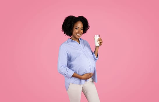 Happy young black pregnant woman in casual with big belly drinks glass of milk