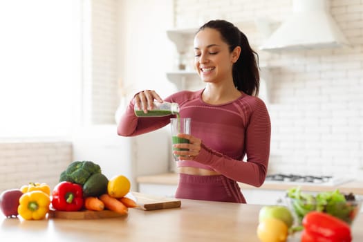 Lady In Sportswear Pouring Green Detox Smoothie In Glass Indoor