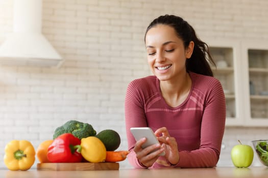 Smiling Fit Woman Using Phone With Cooking Application In Kitchen