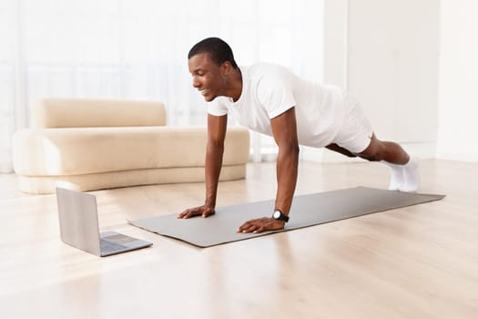 Young athletic black man doing plank exercise with online tutorial