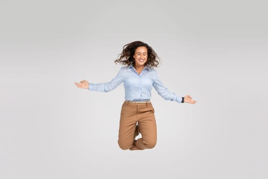 Happy calm young european woman enjoy win jump in air, joy and triumph, with closed eyes