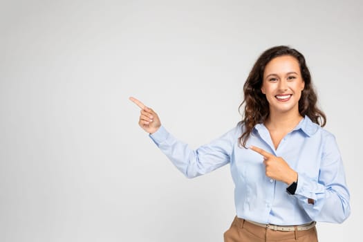 Cheerful young european lady in formal wear pointing fingers at empty space