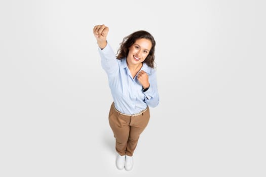 Young woman in studio simulating Superman flight, strong pose with forward fist