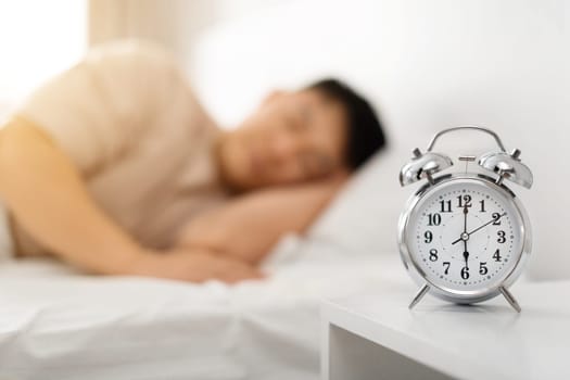 Asian man sleeping through alarm clock in the morning