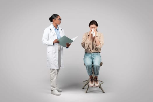 Serious black woman doctor and lady patient cry in clinic office, isolated on gray background studio