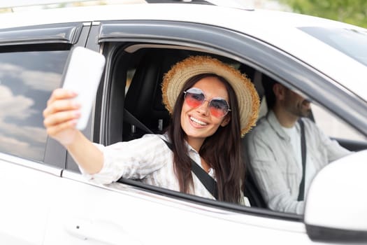 Stylish young woman taking selfie on phone during car ride