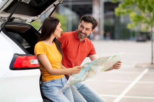 Happy millennial couple having car trip together, reading map