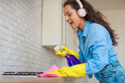 Joyful woman cleaning kitchen, listening to music