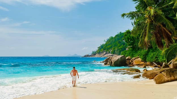 Young men in swimshort on a white tropical beach with palm trees Petite Anse beach Mahe Seychelles